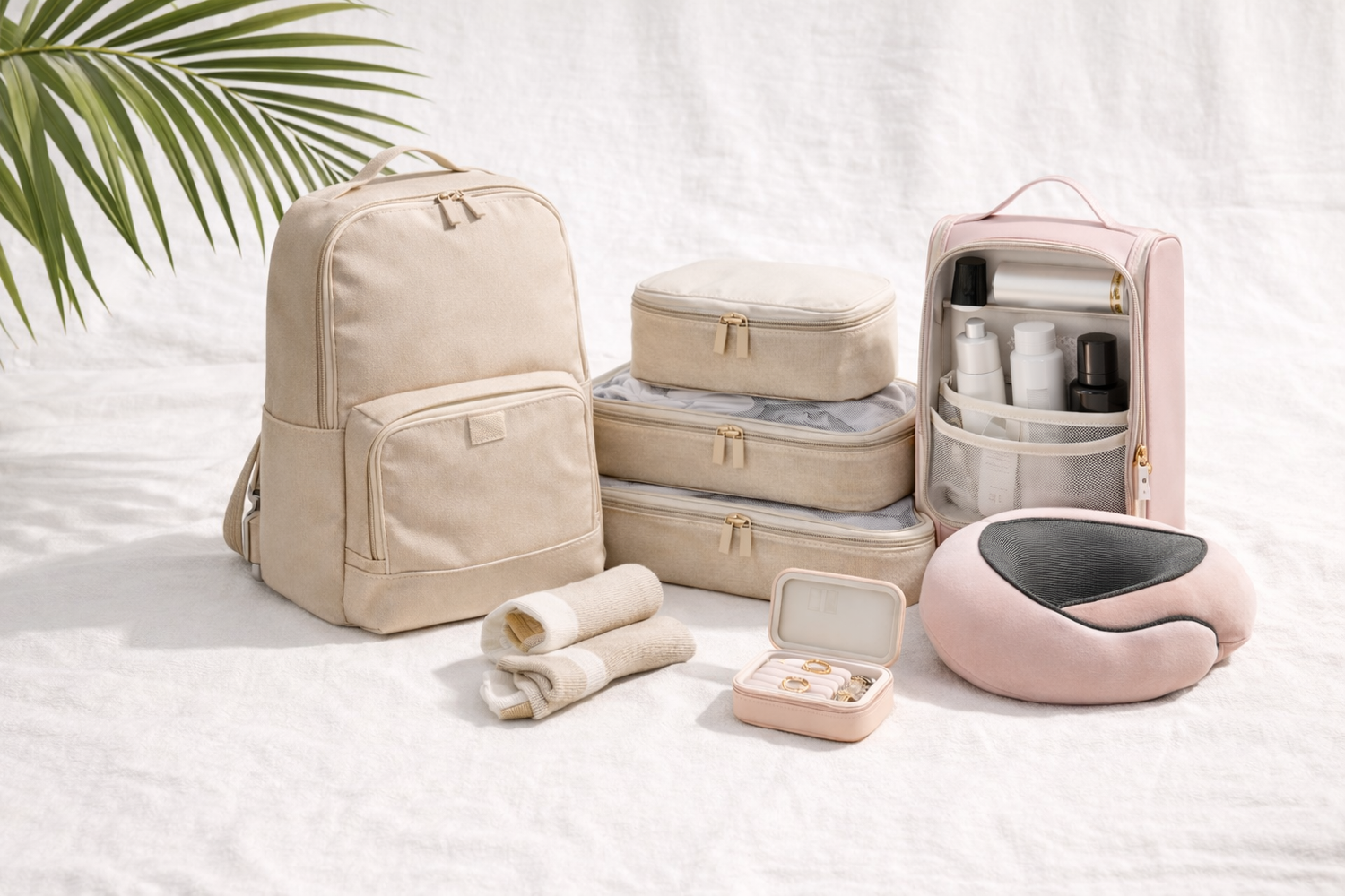 Collection of beige and pink travel bags and accessories on a white surface with a leafy green plant in the corner.