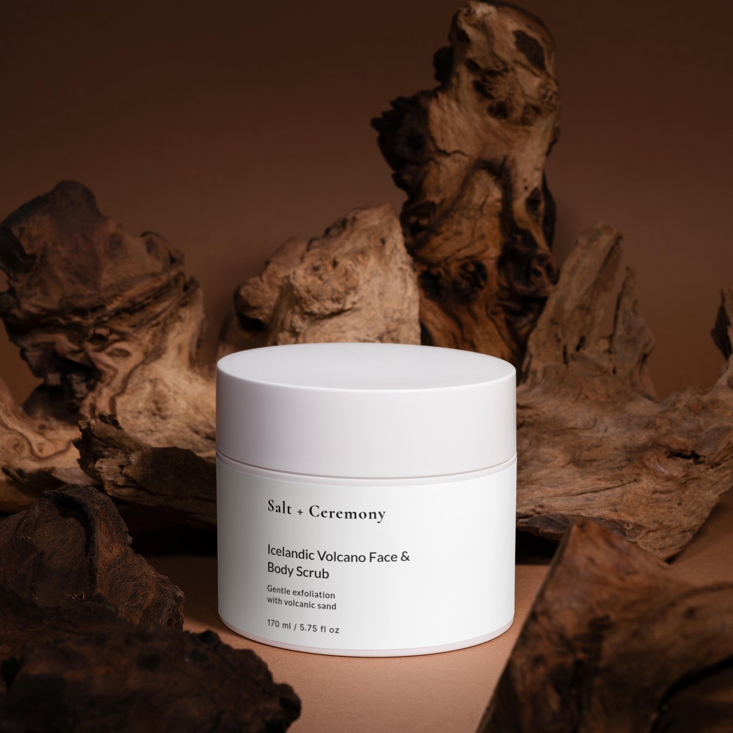 White jar of Salt + Ceremony product on a brown background with natural elements.